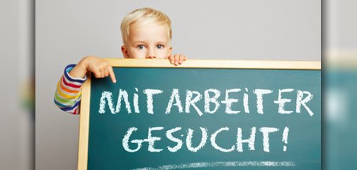 Ein Junge zeigt auf eine Tafel mit der Aufschrift Mitarbeiter gesucht!