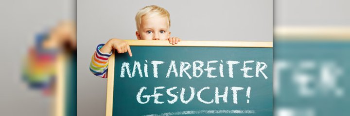 Ein Junge zeigt auf eine Tafel mit der Aufschrift Mitarbeiter gesucht!