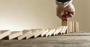 umfallende Dominosteine, die von einer Hand aufgehalten werden 